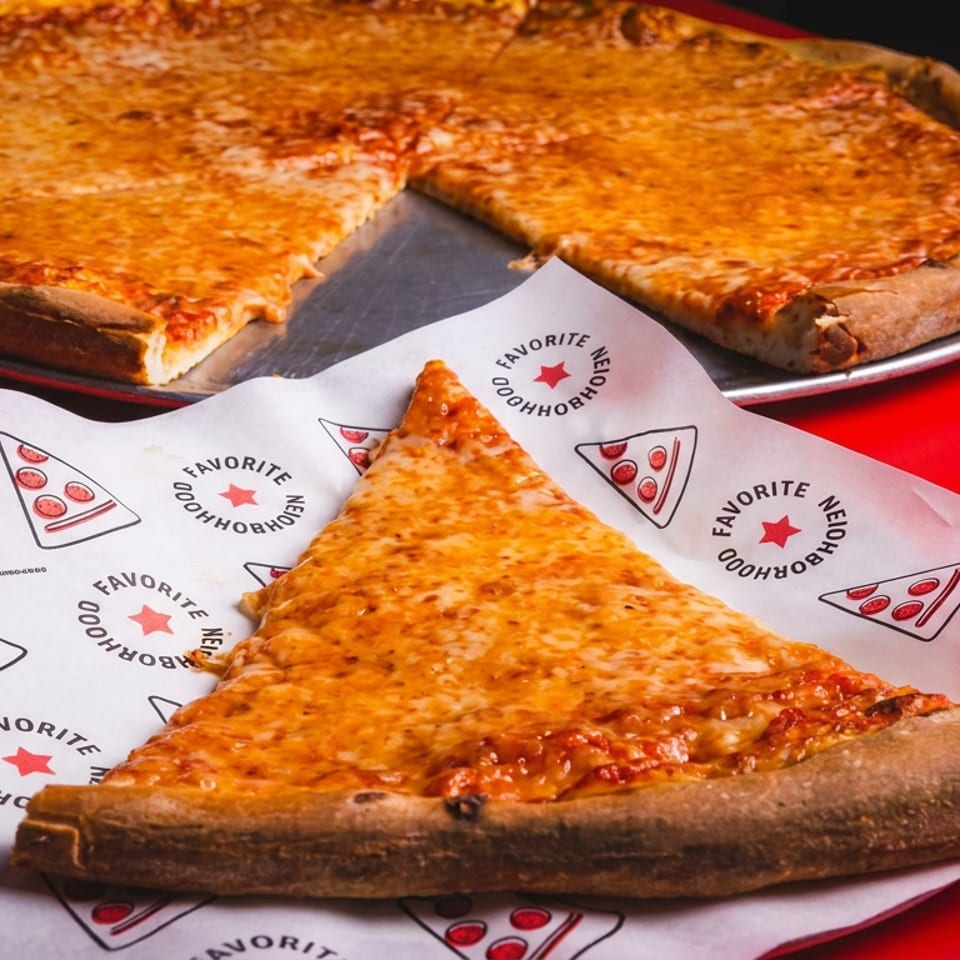 Cheese pizza slice on branded paper in front of a whole deep-dish pizza with a slice removed.
