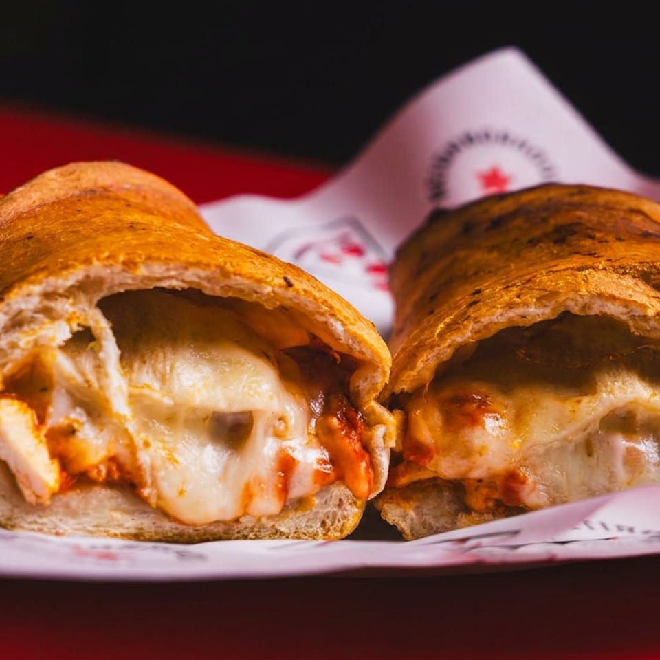 Two toasted sandwich rolls filled with melted cheese and savory meat, served on branded paper.