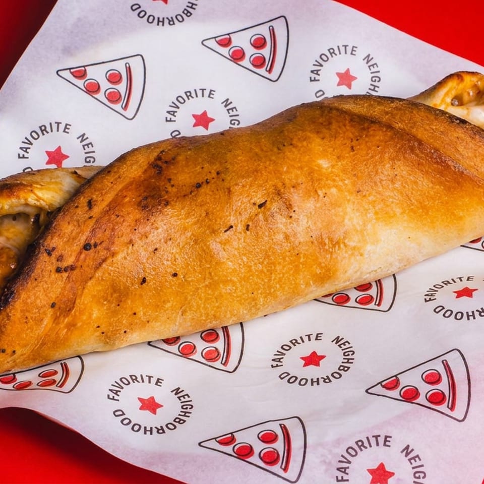 Golden-brown stuffed calzone with toasted edges rests on branded paper against a bright red background.