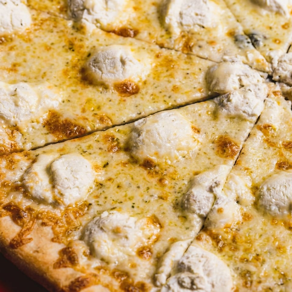 Close-up of sliced cheese pizza topped with mushrooms on a dark surface beside a red background.